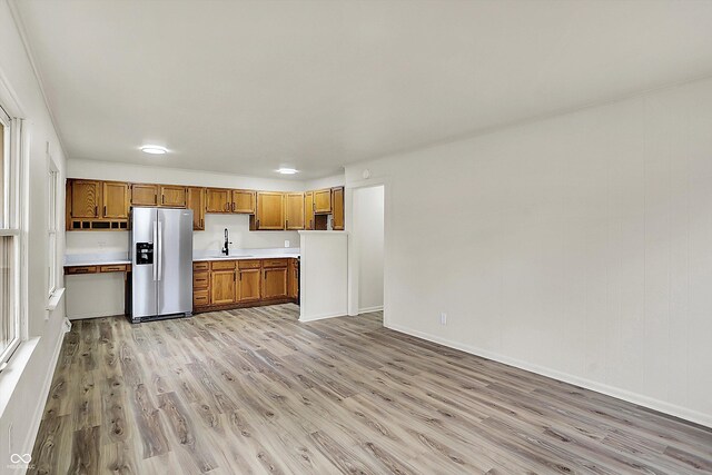 kitchen with stainless steel fridge, brown cabinetry, light countertops, light wood-type flooring, and a sink