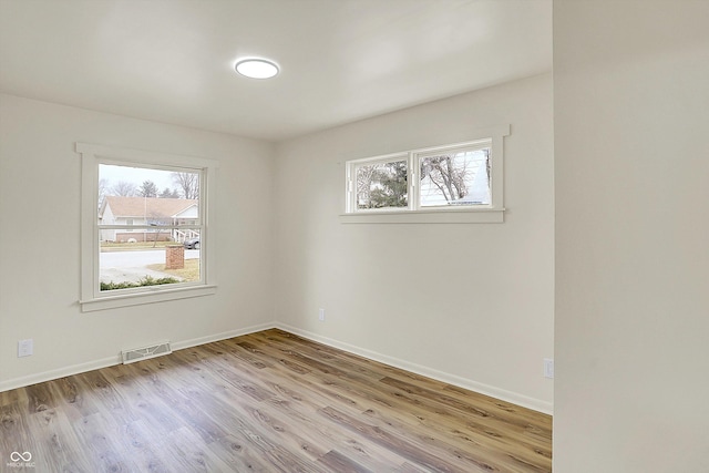 unfurnished room with a healthy amount of sunlight, baseboards, visible vents, and wood finished floors