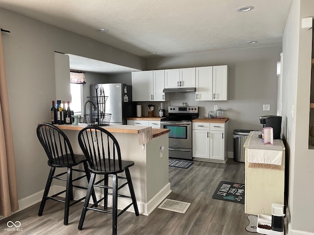 kitchen with under cabinet range hood, a peninsula, wood counters, appliances with stainless steel finishes, and dark wood-style floors