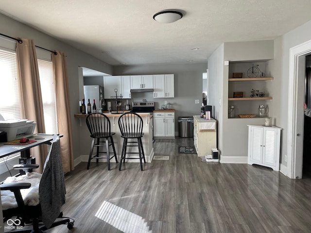 kitchen featuring appliances with stainless steel finishes, dark wood-type flooring, white cabinetry, under cabinet range hood, and a kitchen bar