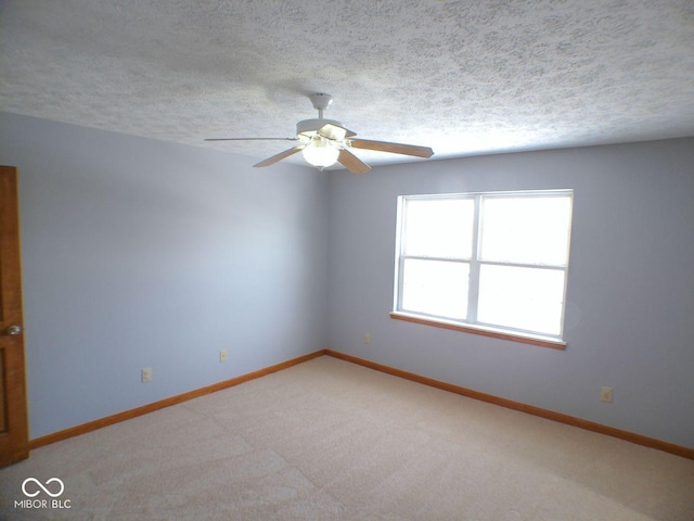 empty room with a ceiling fan, baseboards, a textured ceiling, and light colored carpet