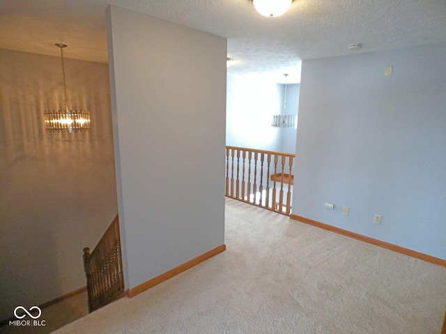 hall with carpet floors, a textured ceiling, baseboards, and a notable chandelier