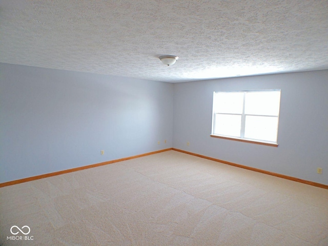 spare room with light colored carpet, a textured ceiling, and baseboards