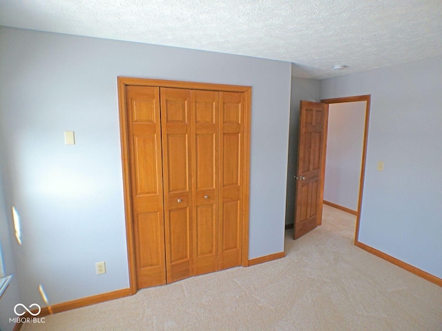 unfurnished bedroom featuring a textured ceiling, baseboards, a closet, and light colored carpet