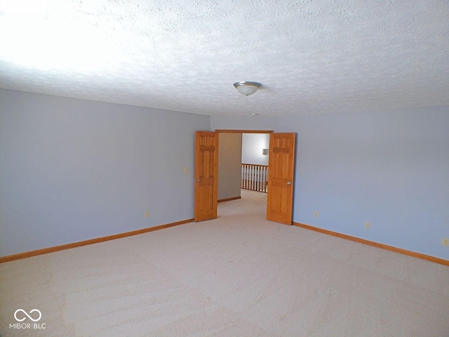 spare room featuring baseboards, a textured ceiling, and light colored carpet