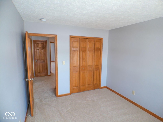 unfurnished bedroom with a textured ceiling, baseboards, a closet, and light colored carpet