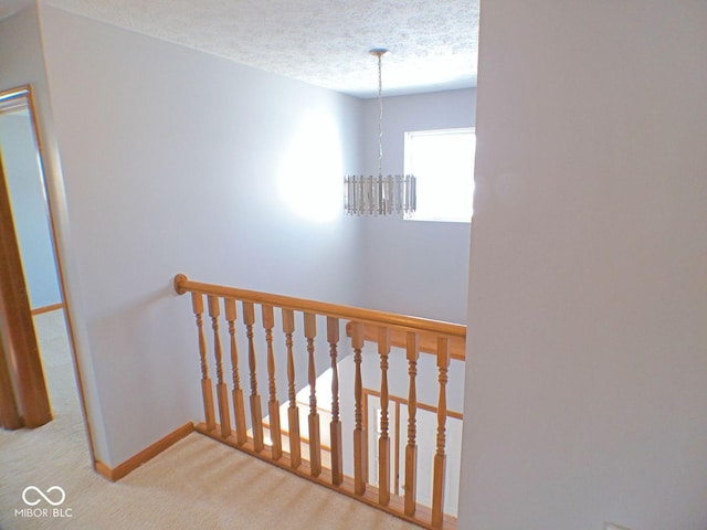 stairway featuring a textured ceiling, carpet floors, a chandelier, and baseboards