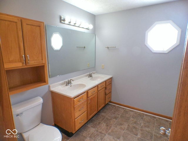 bathroom featuring double vanity, a sink, toilet, and baseboards