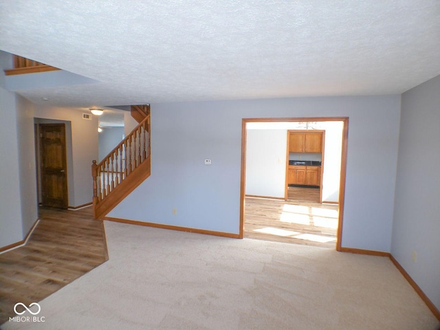 empty room with stairs, a textured ceiling, light carpet, and baseboards