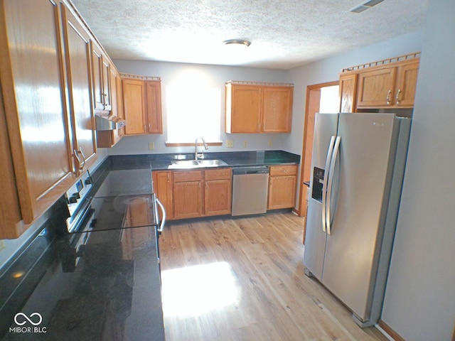 kitchen featuring a textured ceiling, light wood-style flooring, a sink, exhaust hood, and appliances with stainless steel finishes