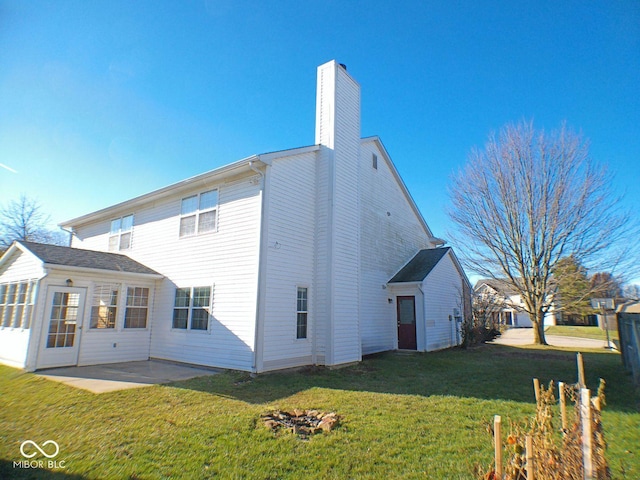 rear view of property featuring a chimney, a lawn, and a patio area