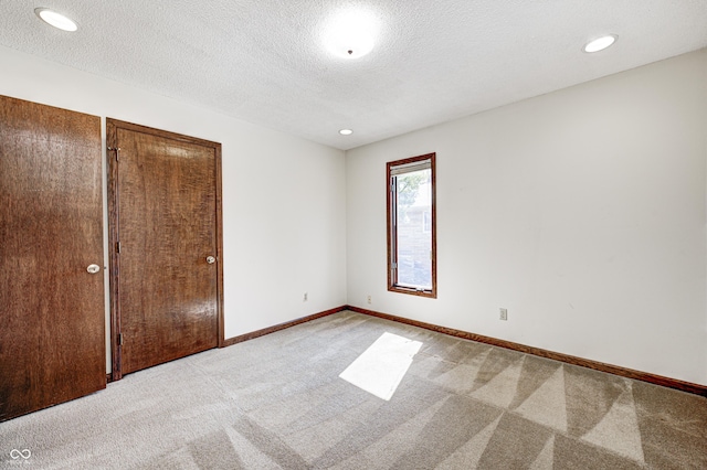 unfurnished bedroom with recessed lighting, light colored carpet, a textured ceiling, and baseboards