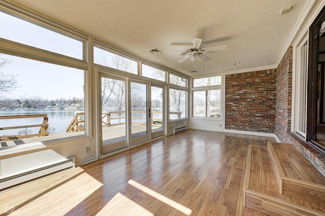 unfurnished sunroom with a baseboard heating unit, a ceiling fan, and a water view