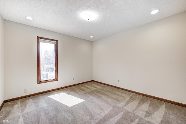 empty room with light carpet, a textured ceiling, and baseboards