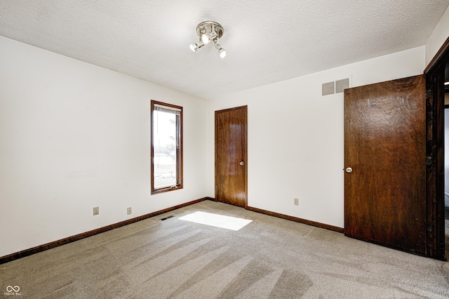 empty room with baseboards, visible vents, carpet floors, and a textured ceiling