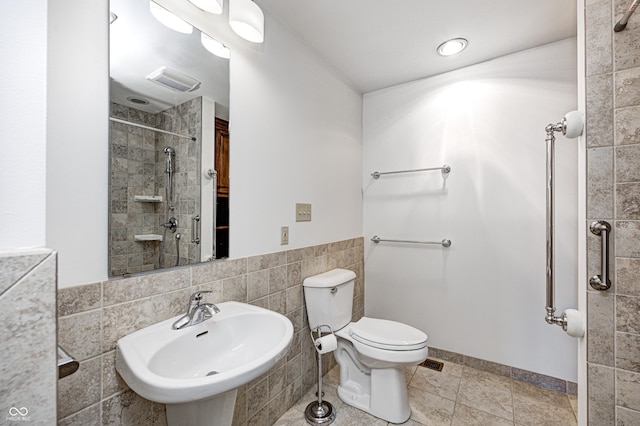 full bathroom featuring visible vents, a tile shower, a sink, tile walls, and toilet