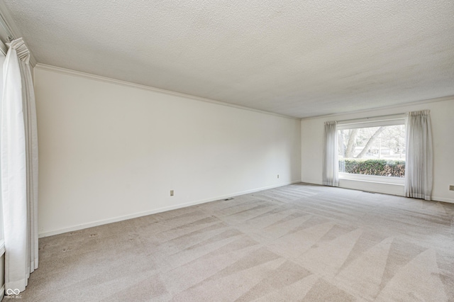 spare room with light carpet, a textured ceiling, crown molding, and baseboards