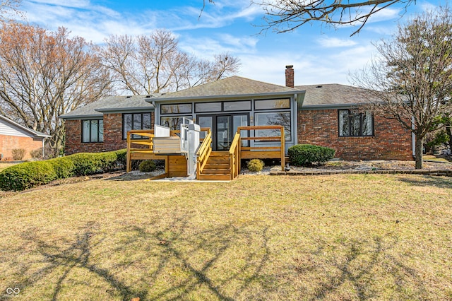 rear view of house with a yard, brick siding, a sunroom, and a chimney