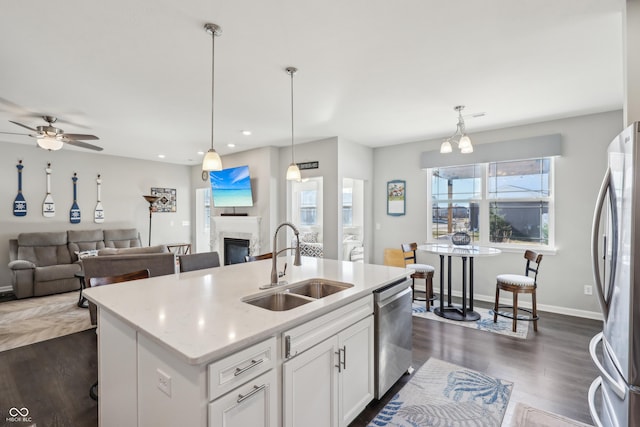 kitchen featuring appliances with stainless steel finishes, dark wood-style floors, a glass covered fireplace, white cabinetry, and a sink