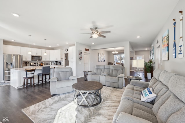 living room with recessed lighting, ceiling fan with notable chandelier, baseboards, and dark wood-style flooring