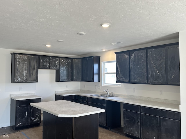 kitchen featuring a center island, visible vents, a sink, a textured ceiling, and dark cabinets