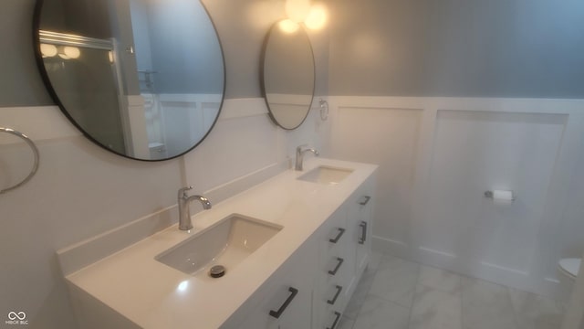 bathroom with a sink, a wainscoted wall, marble finish floor, and double vanity