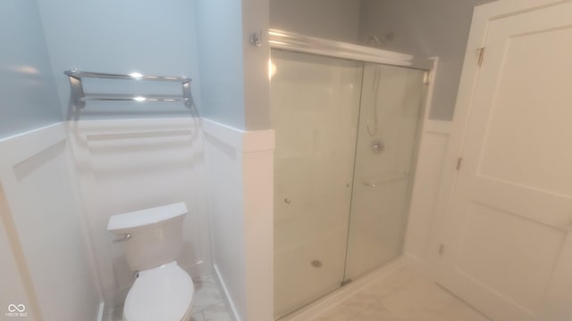 bathroom featuring a wainscoted wall, toilet, and a stall shower