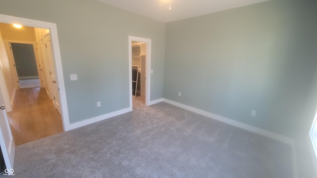 unfurnished bedroom with a walk in closet, carpet, a closet, and baseboards