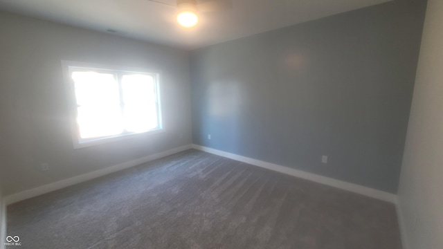 unfurnished room with baseboards and dark colored carpet