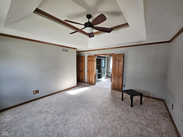 carpeted spare room with visible vents, a tray ceiling, baseboards, and ornamental molding