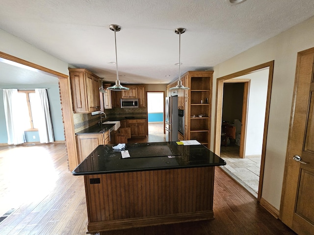 kitchen with brown cabinetry, a kitchen island, appliances with stainless steel finishes, wood finished floors, and open shelves