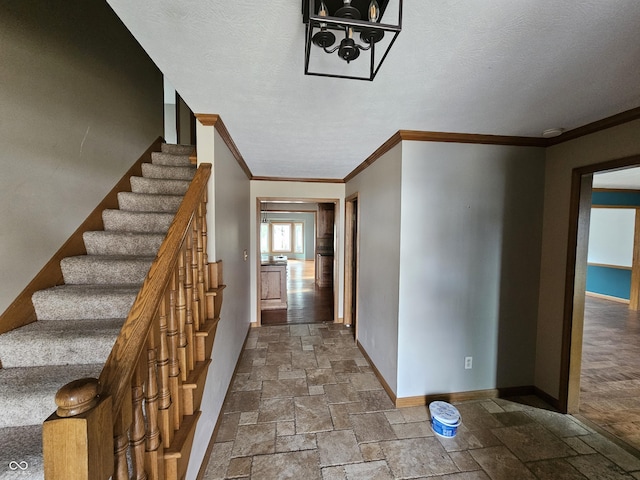 hallway featuring ornamental molding, stone tile flooring, a textured ceiling, and baseboards