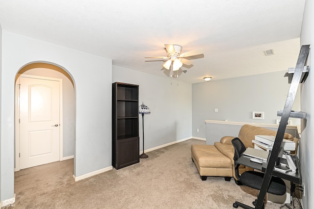 office area featuring arched walkways, light colored carpet, visible vents, ceiling fan, and baseboards