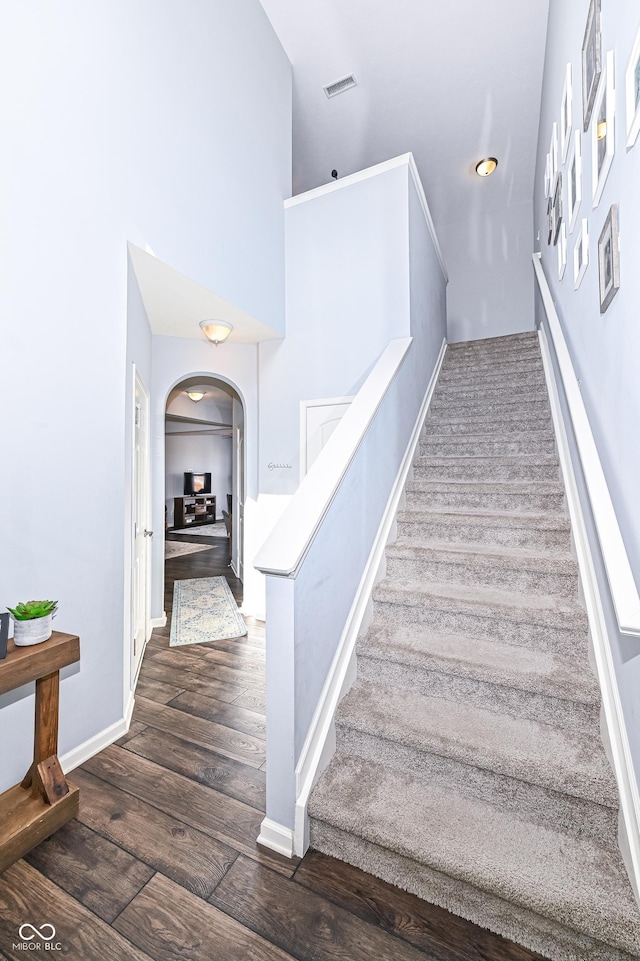 staircase featuring baseboards, visible vents, arched walkways, a towering ceiling, and wood finished floors