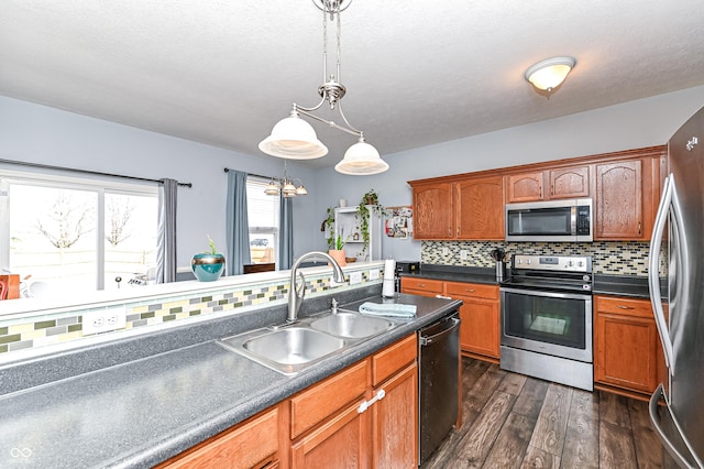 kitchen featuring dark wood finished floors, decorative backsplash, dark countertops, stainless steel appliances, and a sink