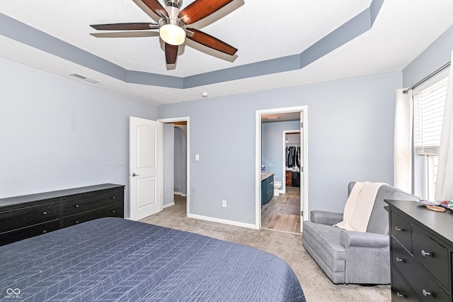 bedroom with visible vents, baseboards, a ceiling fan, light colored carpet, and a tray ceiling