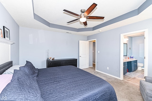 bedroom featuring light carpet, baseboards, visible vents, a raised ceiling, and ensuite bath