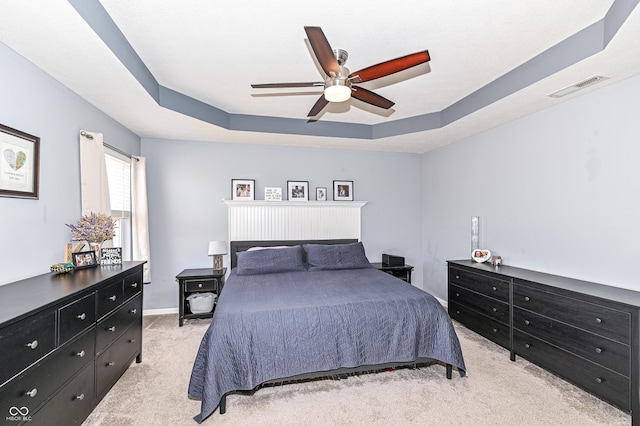 bedroom with visible vents, a raised ceiling, baseboards, light colored carpet, and ceiling fan