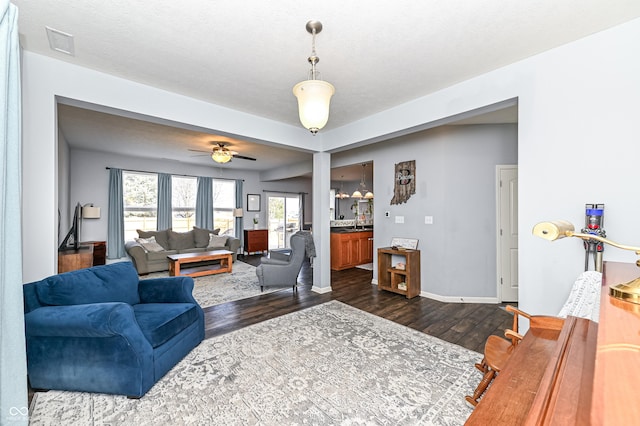 living room with ceiling fan, dark wood-type flooring, visible vents, and baseboards