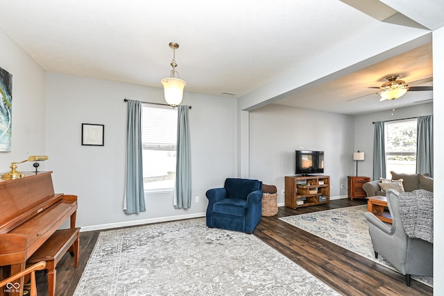 living area with dark wood-type flooring, baseboards, and a ceiling fan