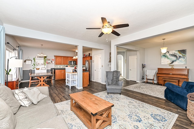 living area with dark wood-style floors, ceiling fan, arched walkways, and baseboards