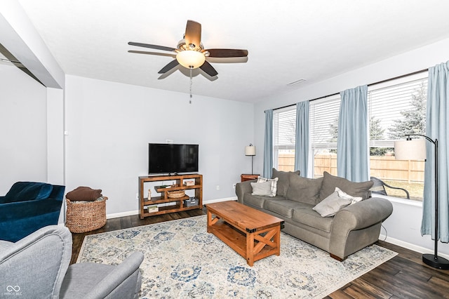 living room with ceiling fan, baseboards, and dark wood-type flooring