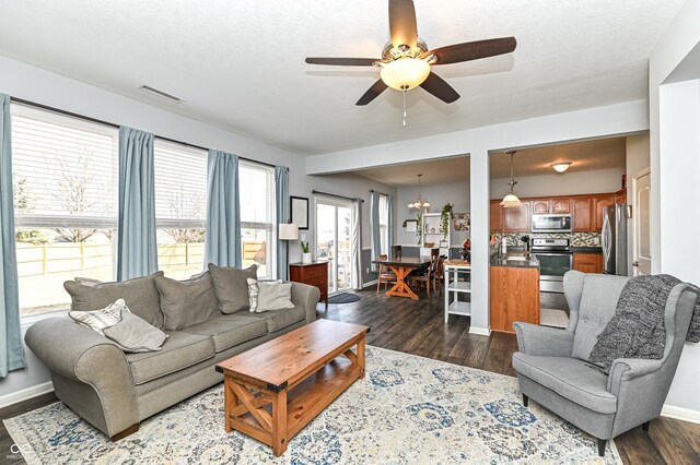 living room with baseboards, visible vents, dark wood-type flooring, a textured ceiling, and ceiling fan with notable chandelier