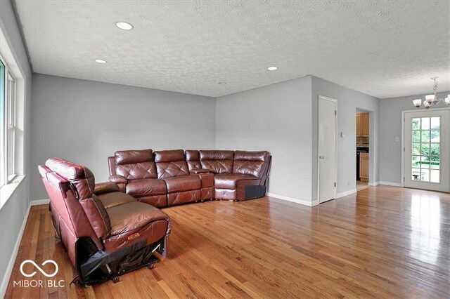 living area with a chandelier, a textured ceiling, baseboards, and wood finished floors