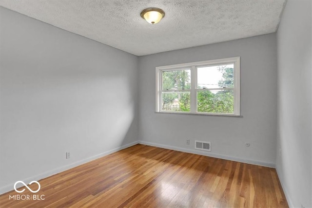 spare room featuring hardwood / wood-style floors, baseboards, visible vents, and a textured ceiling