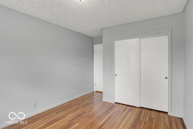 unfurnished bedroom with a textured ceiling, wood finished floors, a closet, and baseboards