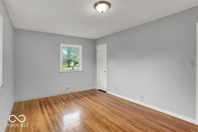 spare room featuring baseboards, wood finished floors, visible vents, and a textured ceiling