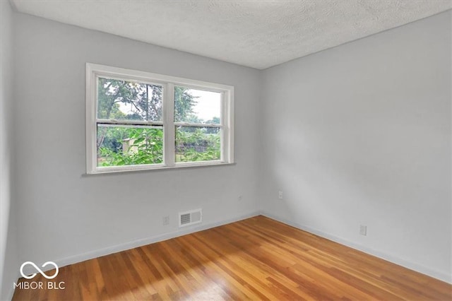 empty room with visible vents, baseboards, light wood-style floors, and a textured ceiling