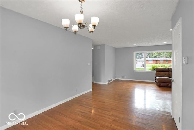 empty room with visible vents, a textured ceiling, wood finished floors, an inviting chandelier, and baseboards