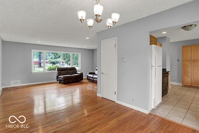 unfurnished living room with visible vents, a textured ceiling, light wood finished floors, baseboards, and a chandelier